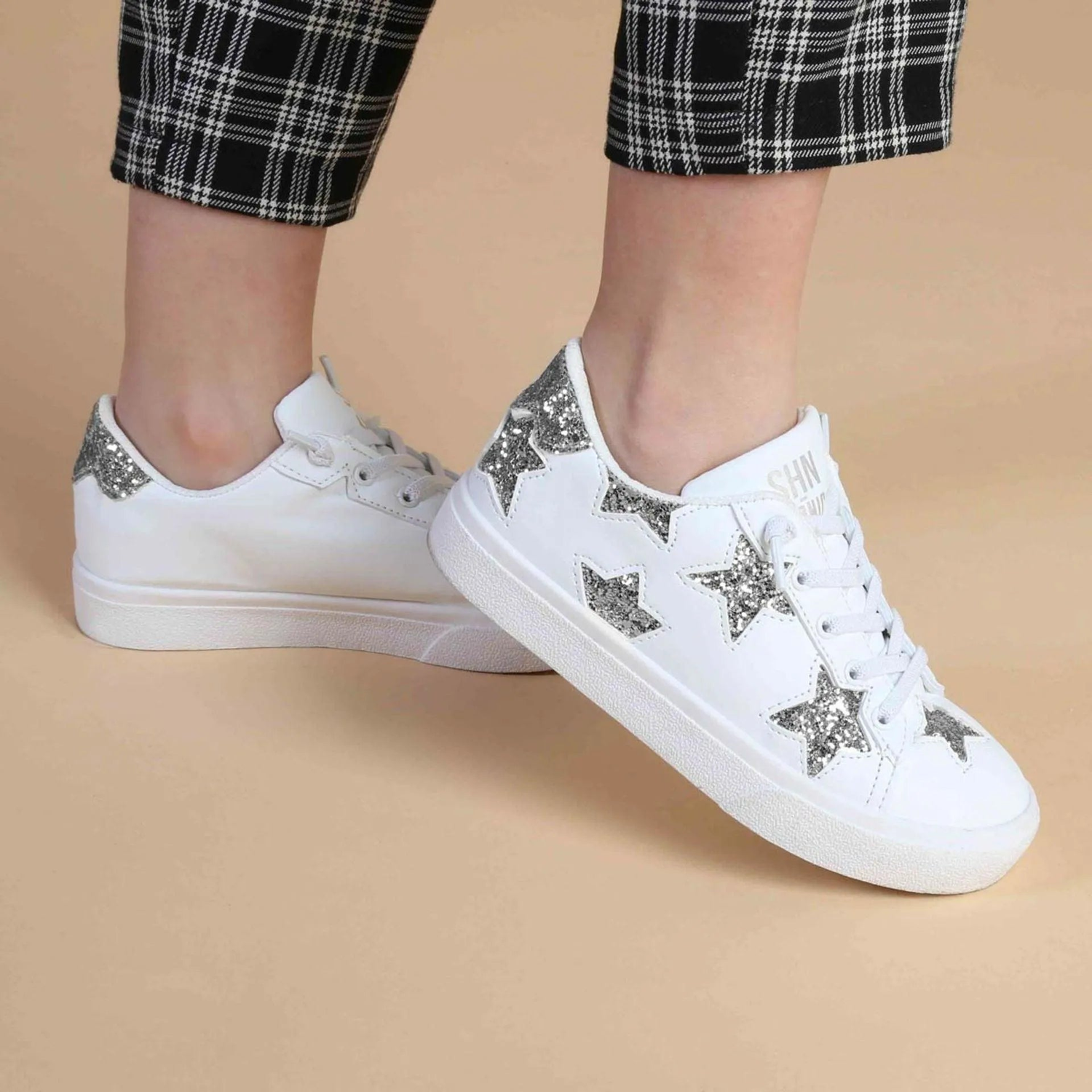 Kids white sneakers with silver glitter star design, plaid pants, beige background