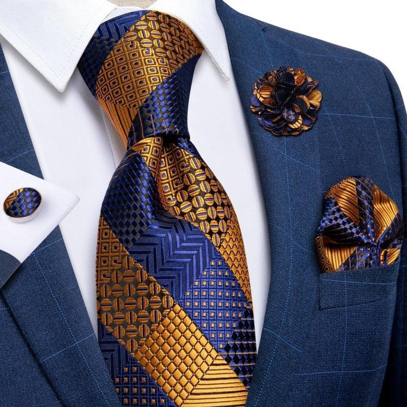 Blue and gold patterned necktie set with matching pocket square, cufflink, and lapel pin on a blue suit